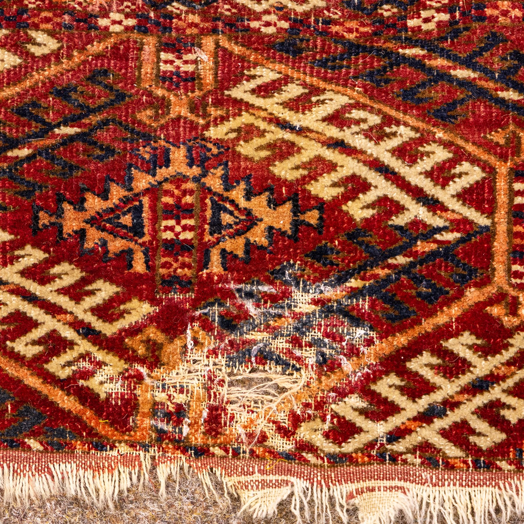 Vintage Bokhara hand-knotted rug, madder field woven in rows of octagonal Tekke guls arranged in vertical columns, each enclosing angular cruciform devices and tribal motifs, divided by narrow indigo lines, within multiple geometric borders incorporating stepped lozenges and latch hook devices, with cotton fringe ends 