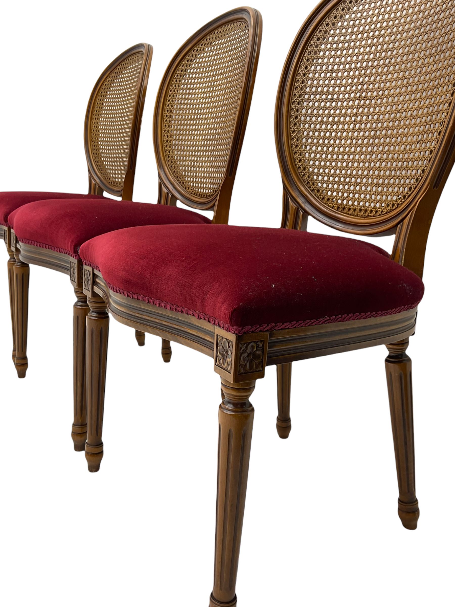Set six French style walnut finish dining chairs, oval cane bergere backs over serpentine seats upholstered in red, flower head carved fluted supports