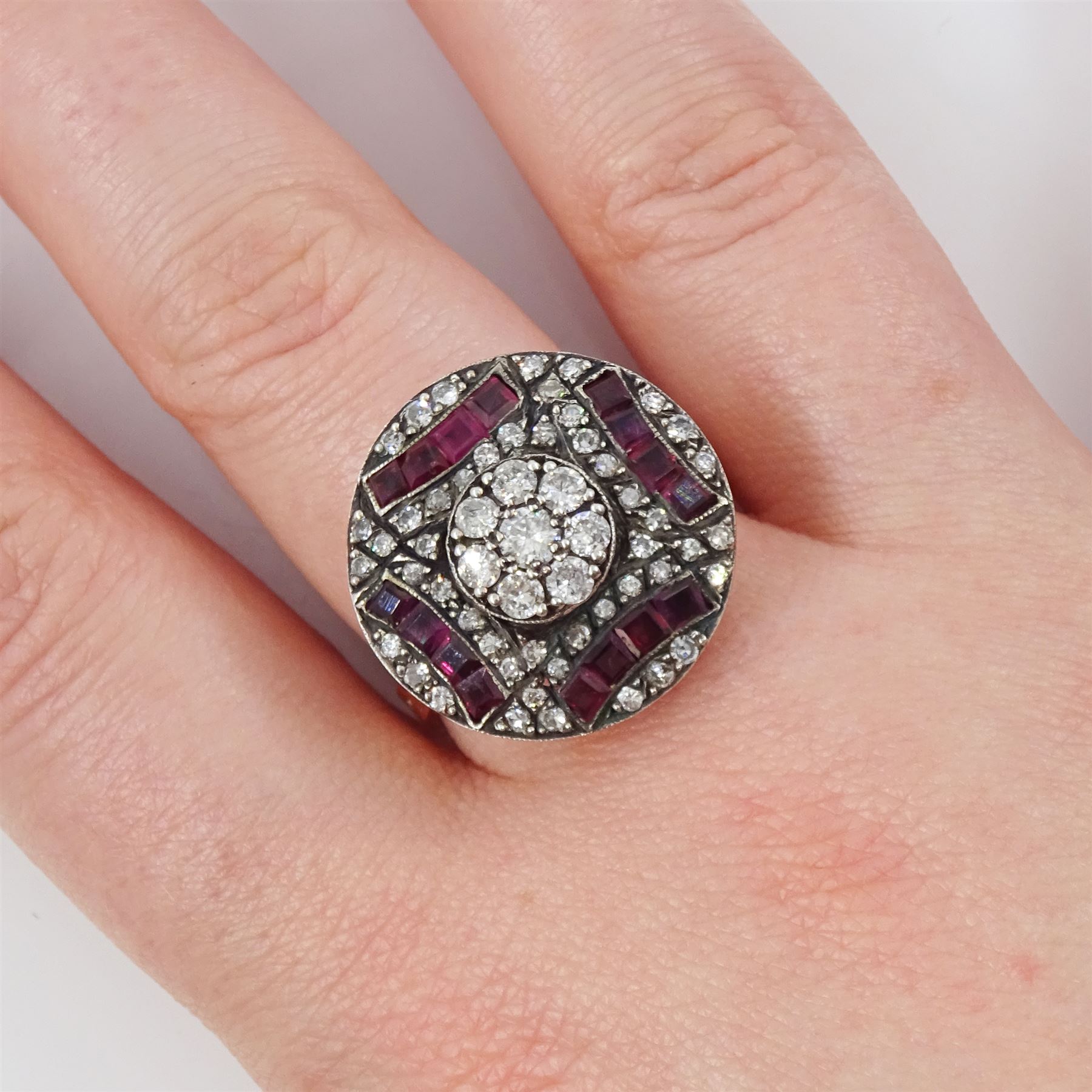 Rose gold and silver ruby and diamond circular ring, the central cluster set with eight round brilliant cut diamonds, with calibre cut ruby and single cut diamond surround, total diamond weight approx 0.90 carat, total ruby weight approx 0.75 carat