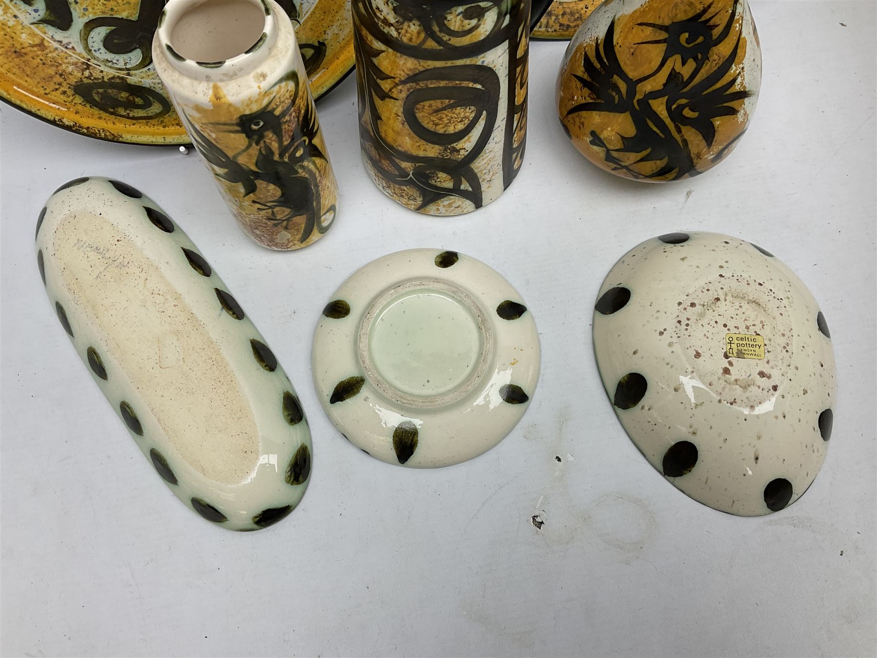 20th century Celtic Pottery, Newlyn, vases of baluster and cylindrical form, ovoid shaped bowl, plates, rectangular shallow dish etc, all decorated with a dark stylised phoenix, modelled with wings outstretched upon sponged ochre, blue and cream ground, together with a plate decorated with a stylised horse and tankard of tapering form (8)