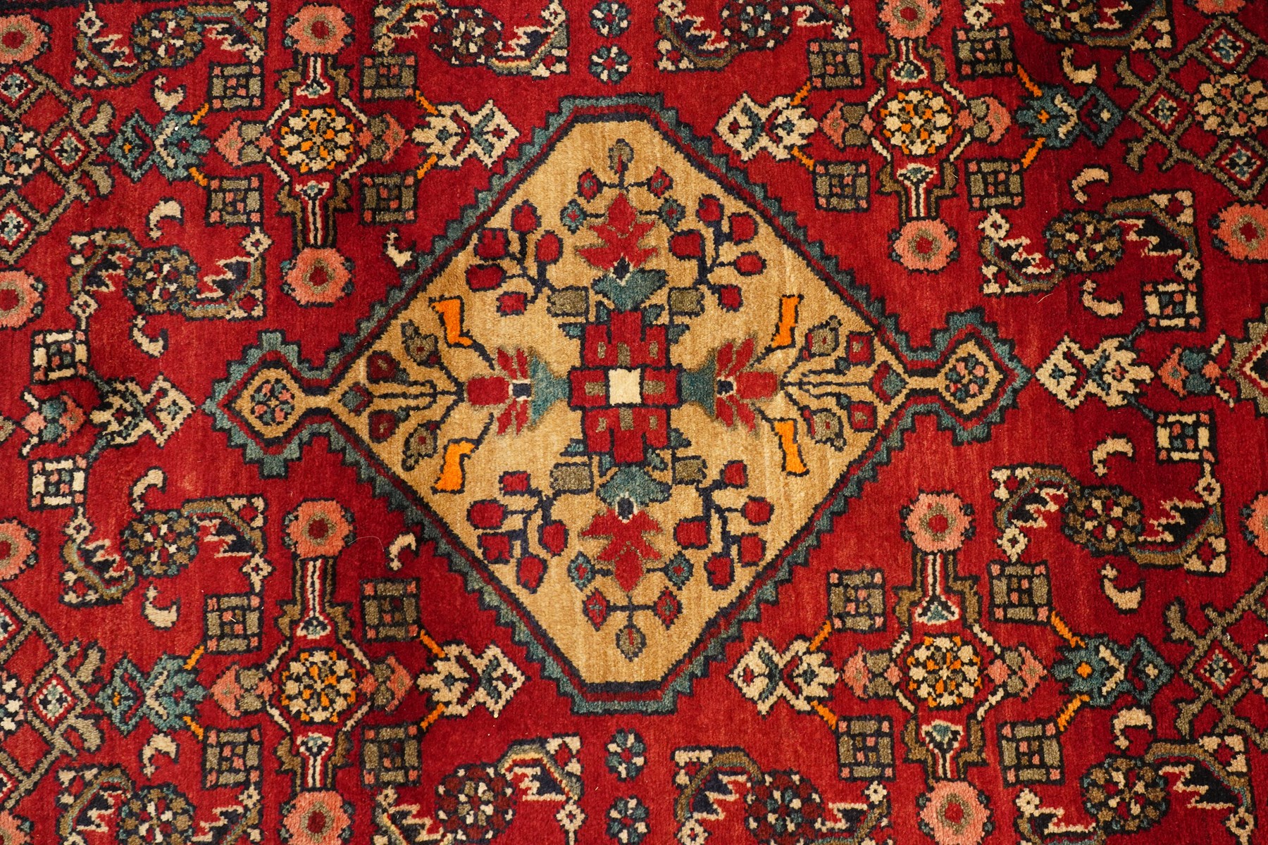 Large Persian Qashqai runner rug, the red ground decorated with navy and ivory lozenge medallions interspersed with stylised floral and geometric motifs, enclosed by an ivory flowerhead border and patterned guard stripes