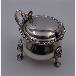 1920's silver mustard pot and cover, of bellied form with oblique gadrooned rim and capped scroll handle, the palmette thumbpiece lifting the slightly domed cover to reveal a blue glass liner, upon three mask mounted shell pad feet, hallmarked Mappin & Webb Ltd, London 1923, H7.5cm, approximate weight excluding liner 4.88 ozt (151.7 grams)