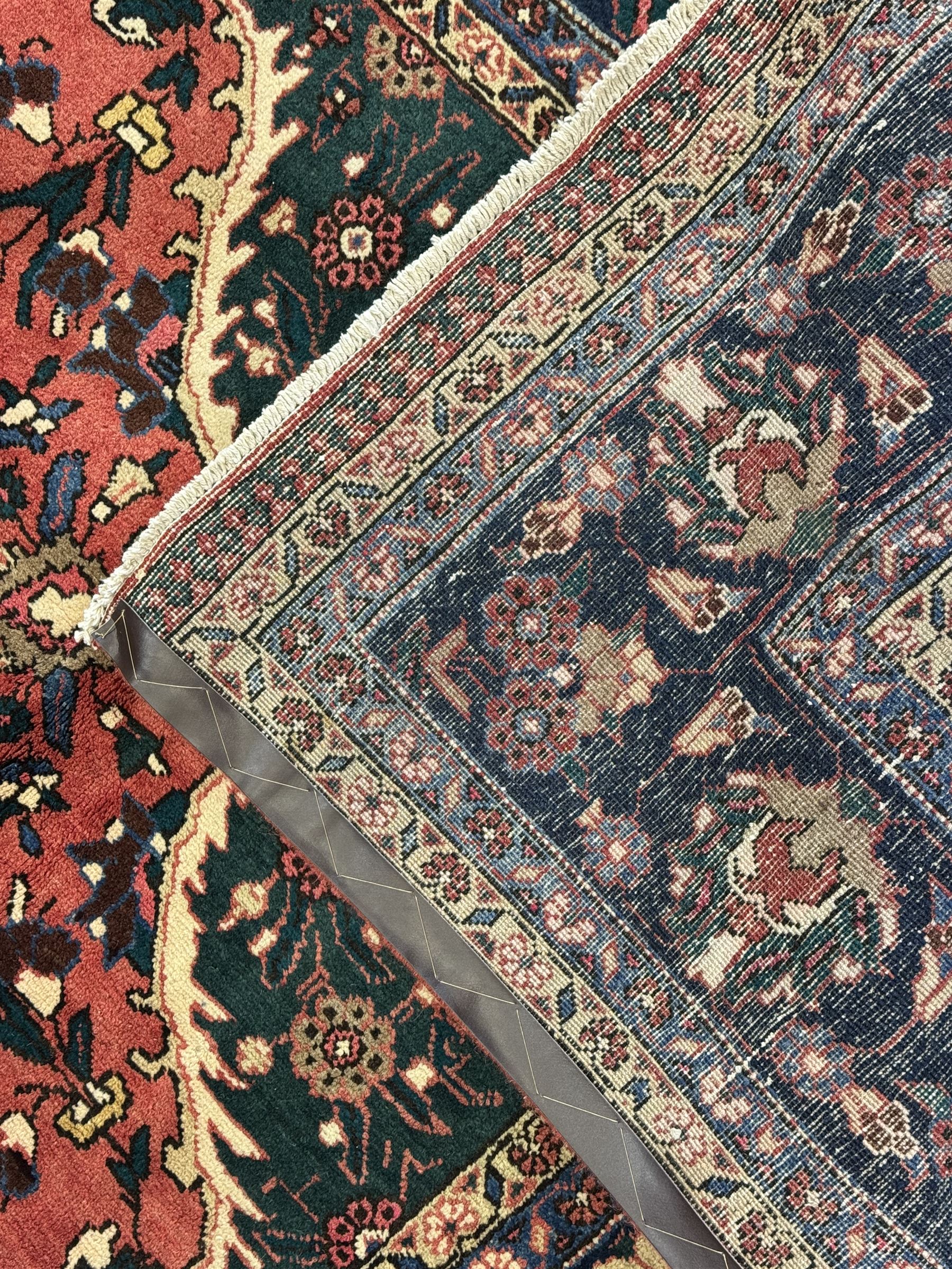 North East Persian Meshed crimson ground carpet, central indigo and green medallion with floral decoration, busy field with trailing foliage and stylised flowers, matching spandrels with floral motifs, indigo border featuring scrolling vines and palmettes, framed by narrow floral guard bands