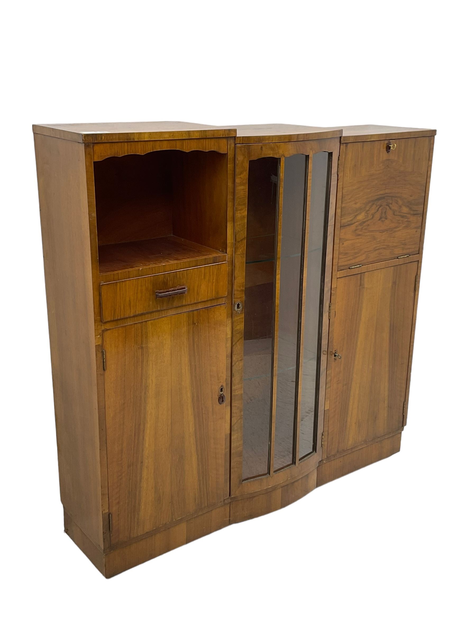 Early 20th century walnut side cabinet, enclosed by central bowed and glazed door, fitted with drawer, two cupboards and fall front, on plinth base