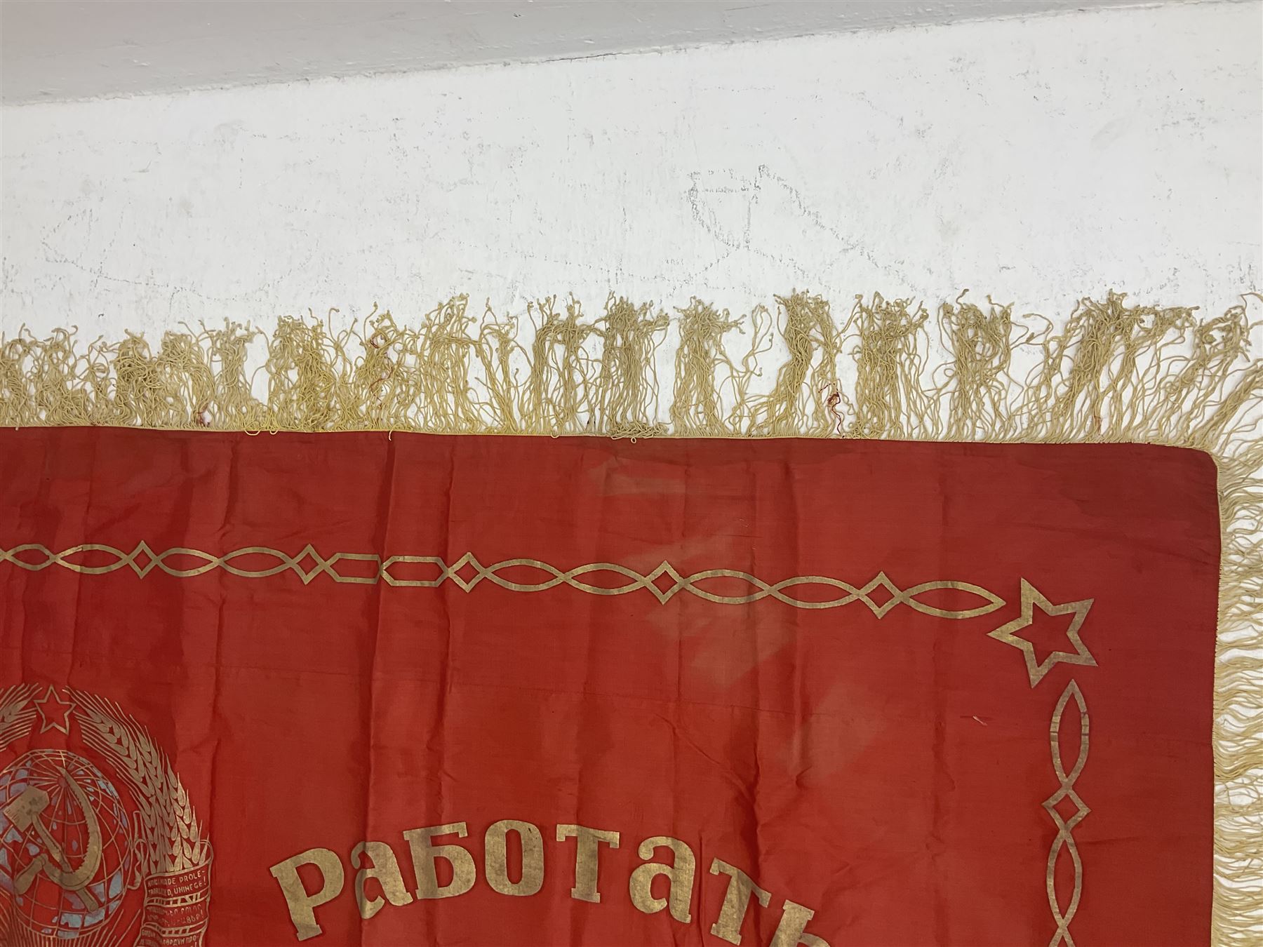 1970s Soviet banner printed in gold on a red ground, roughly translates as 'Transferable Banner - To the winner in the Socialist Competition' and 'Work Study Live by Communism' verso; wreath of wheat ears to either side; tassels on three sides 110 x 155cm