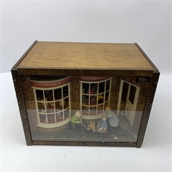A 1/12th scale diorama of a toy shop window, depicting three children outside 'Adelaide's Toy Shop', the windows displaying assorted toys, including dolls, skittles, teddy bears, rocking horse, dolls house, etc. 

H29cm L40cm D26cm.