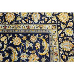 Central Persian Kashan hand-knotted carpet, deep indigo field with a densely all-over arrangement of scrolling floral vines, palmettes, and flowering sprays, in soft ivory, pale blue, and warm gold tones, principal ivory border with a continuous meandering vine of stylized palmettes, and floral motifs, flanked by multiple narrow guard borders, with cotton fringe ends 