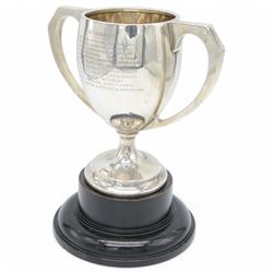 1920s silver twin handled trophy with engraving to body, upon circular foot and ebonised wooden plinth, total height H20cm