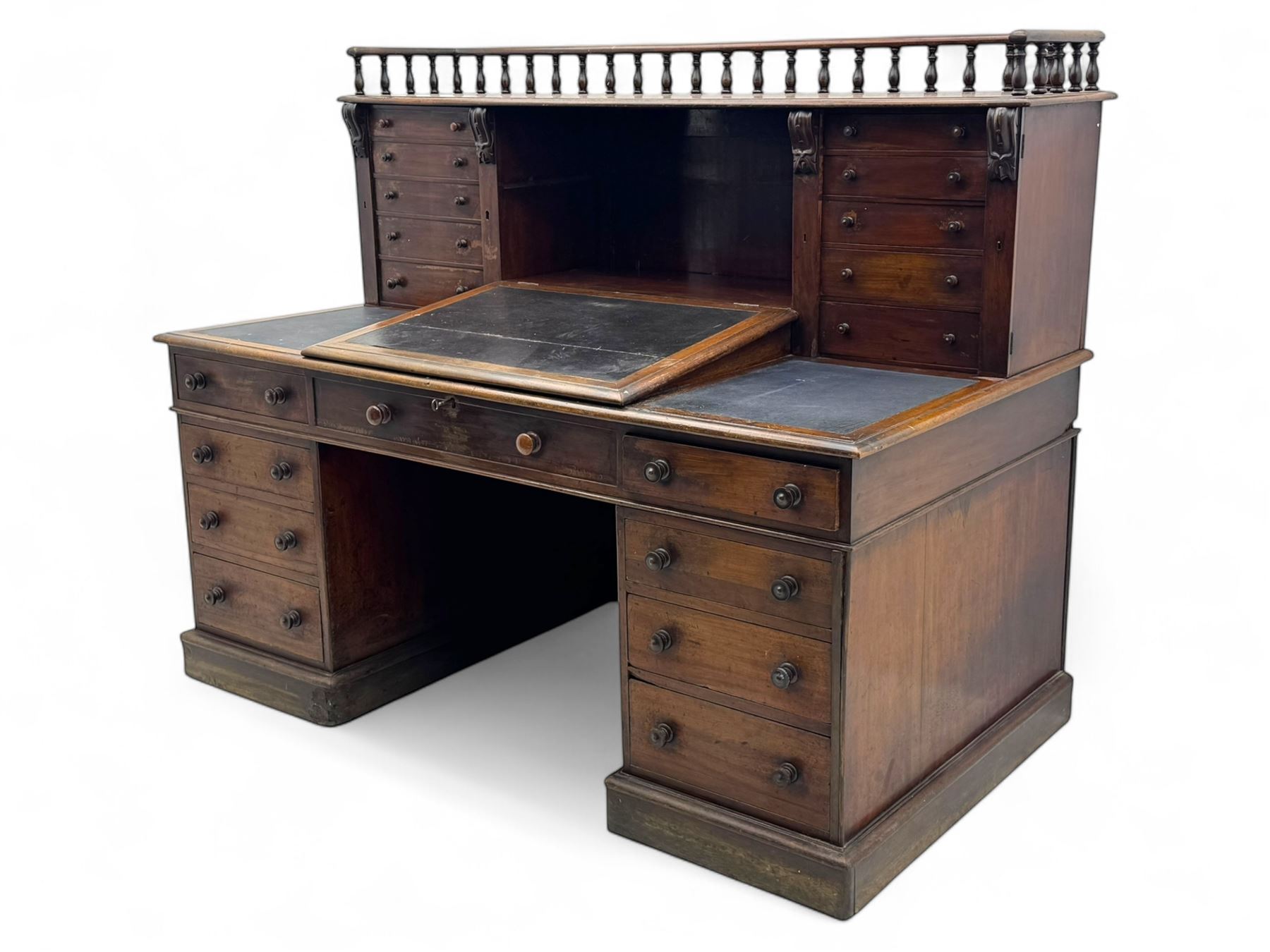 Large Victorian mahogany Registry/Dickens’ desk, spindle gallery top, one side with five small drawers and the other with blind cupboard drawer, revealing pigeon holes with scroll carved locking side bars on either side, above a hinged and leathered writing slope with three drawers and pigeon holes underneath, above a central locking drawer with key, the pedestals each with four drawers and  turned knob handles, separates into four parts for transport