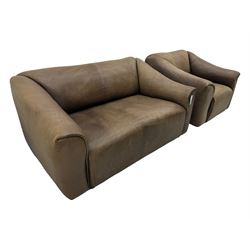 Mid-20th century two seater sofa, upholstered in soft brown leather with visible patina, curved arms and low back, on concealed supports (W138cm, D86cm, H72cm); matching armchair (W84cm, D86cm, H72cm)