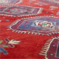 Caucasian Kazak rug, red field decorated with a column of stepped hexagonal medallions in blue, ivory, and crimson, flanked by stylized floral and geometric motifs, enclosed by multiple borders of rosettes and hooked designs 