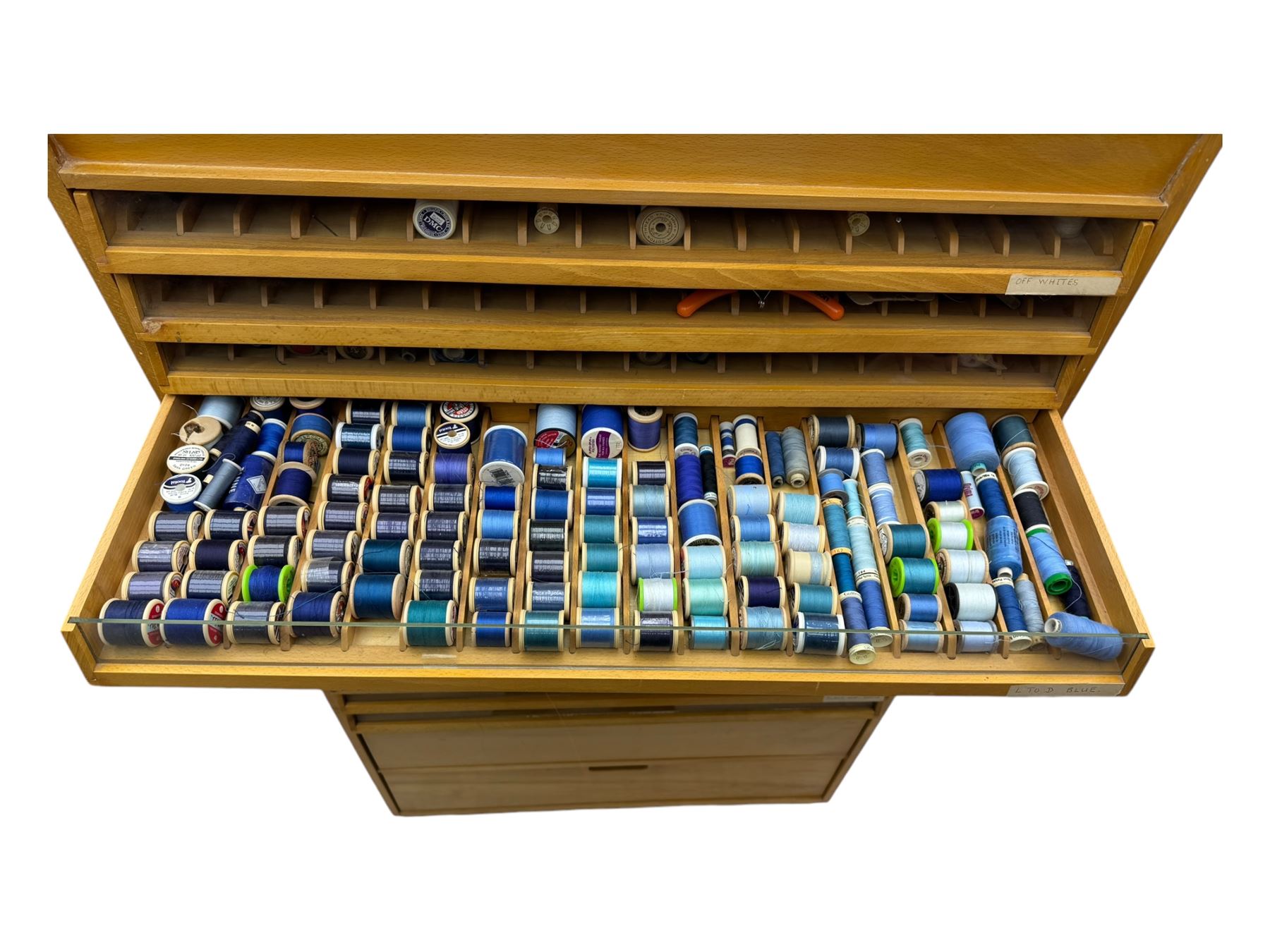 Large beech haberdashery thread storage cabinet, rectangular form with fourteen glass-fronted sloping drawers housing an extensive array of thread spools in assorted colours, over two larger drawers, raised on plinth base