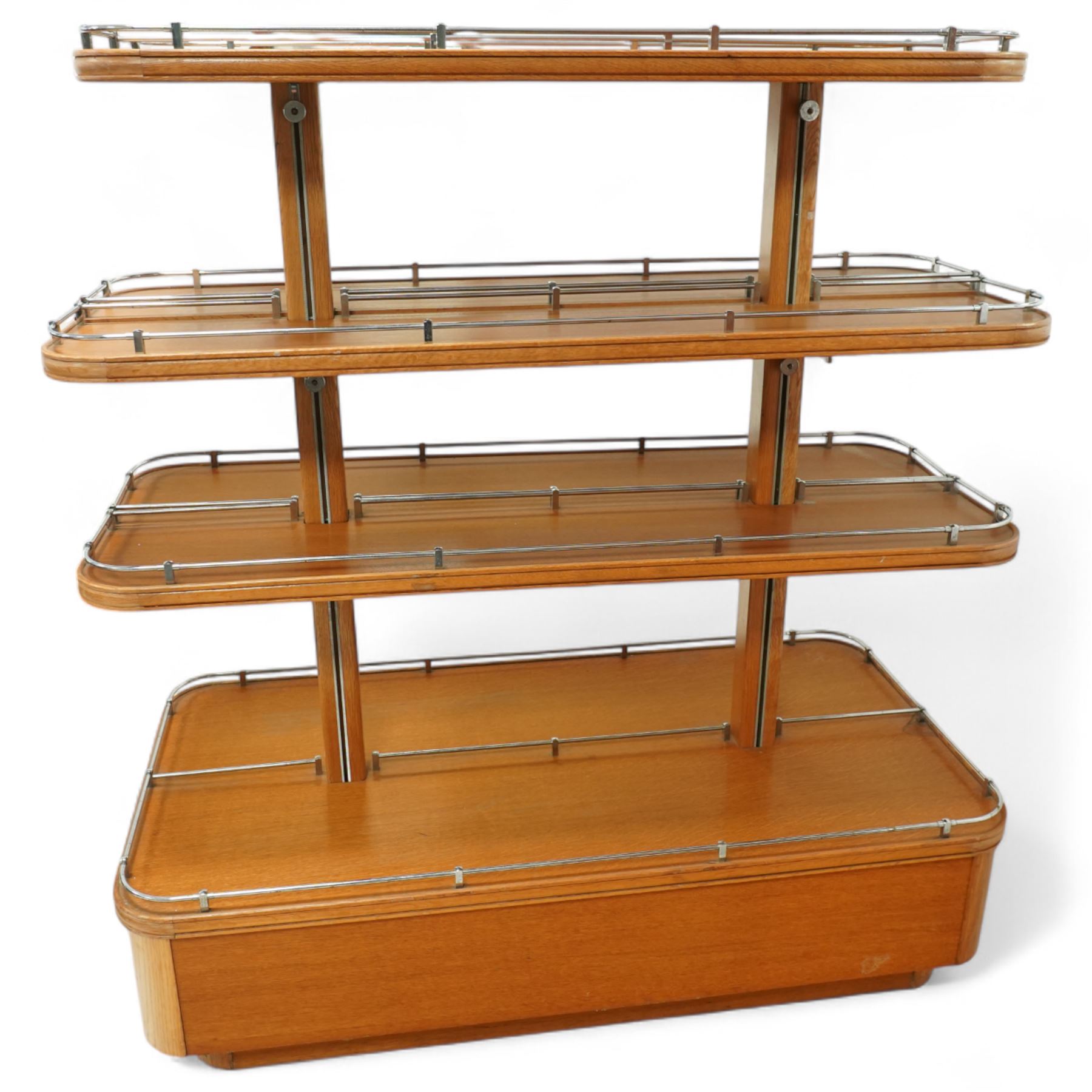 Mid-20th century retail display stand, of stepped rectangular tiered form with four graduated adjustable shelves, each with rounded corners and fitted with tubular chrome safety rails, supported by central chrome-mounted wooden uprights over a plinth base