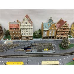 Table top 'N' gauge continental scenic layout as a split level town with various loops of track, station with numerous platforms, engine shed, assorted buildings, roads with motor vehicles and figures, tunnels, trees, river with bridge, tram depot etc 122 x 52cm