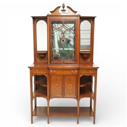 Edwardian Sheraton Revival inlaid mahogany breakfront cabinet, the broken swan neck pediment with central finial inlaid with cartouche and scrolling floral festoons, the central cabinet fitted with astragal-style glazed door with central urn and swag motif, flanked by arched bevelled mirrors over a shelf and gadrooned bracket over paterae inlays, base fitted with marquetry frieze rawer over a panelled cupboard with intricate inlaid scrolling floral designs, flanked by open shelves, raised on square tapering herringbone inlaid supports united by undertier