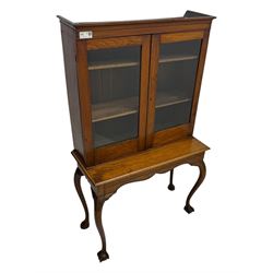 Late 19th century oak display cabinet, rectangular form with a pair of glazed doors enclosing shelves, raised on cabriole supports with carved detailing ending in claw feet