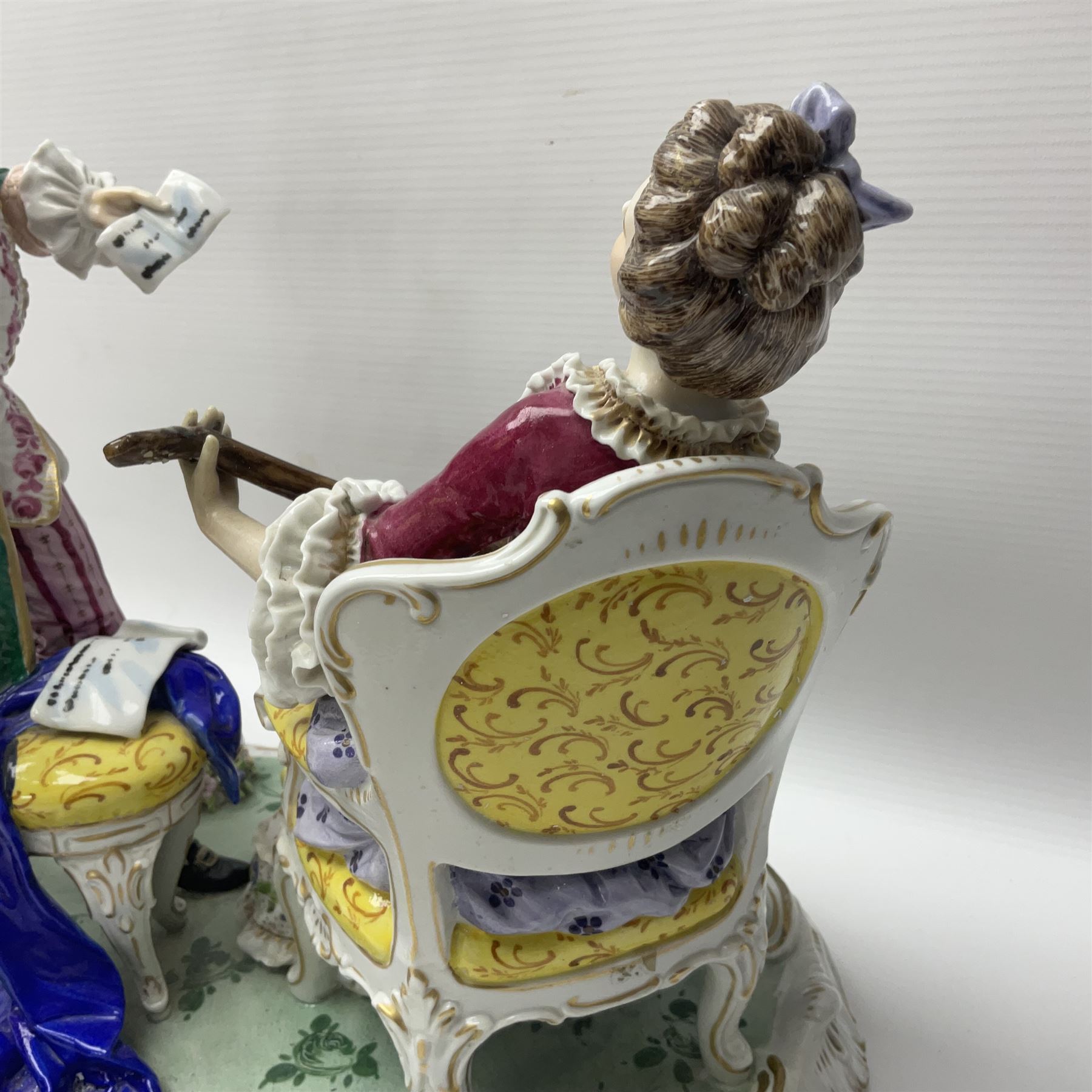 20th century Naples figure group, modelled as a seated female figure playing the lute seated, before a male figure stood holding a sheet of music, each in period dress, upon an oval base with gilt heightened scroll edge, with crowned N mark beneath, H31.5cm L33cm
