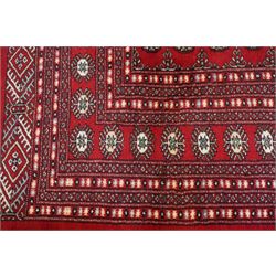 Large crimson ground Afghan Bokhara carpet, the field decorated with repeating Gul and geometric motifs, the multiple guard stripes with further geometric decoration
