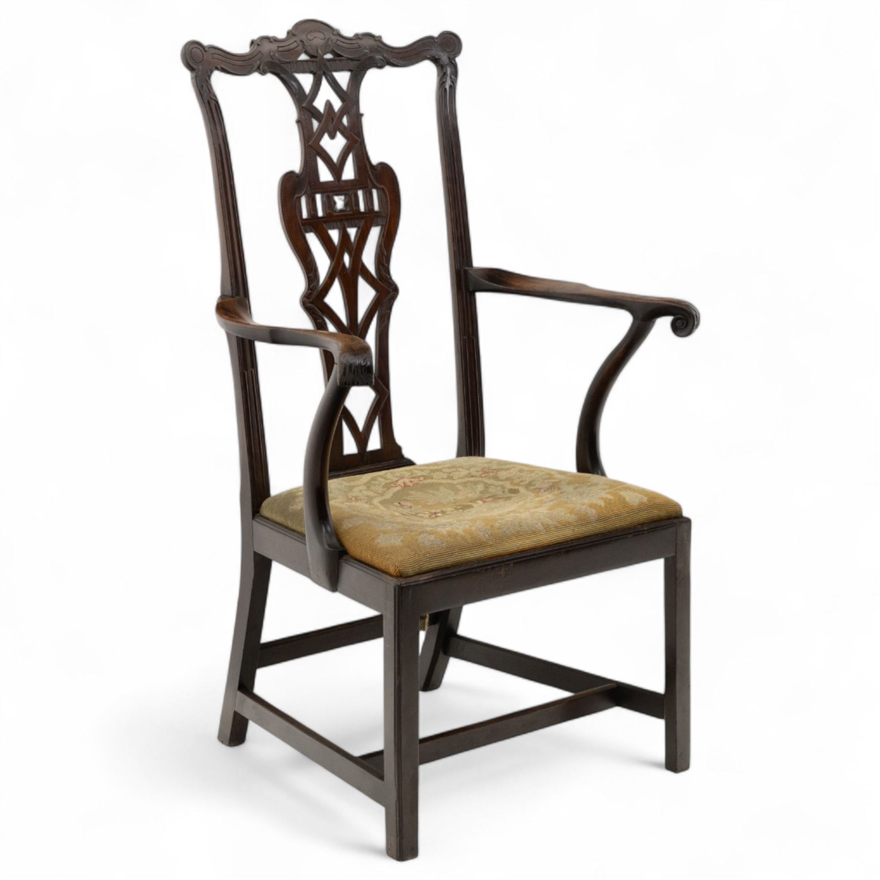 19th-century Chippendale Revival design mahogany oversized high-back armchair, serpentine crest carved top rail above pierced back splat with interlaced ribbon carving and geometric fretwork design, and outward scrolling arms above drop-in needlework seat on square chamfered legs 
