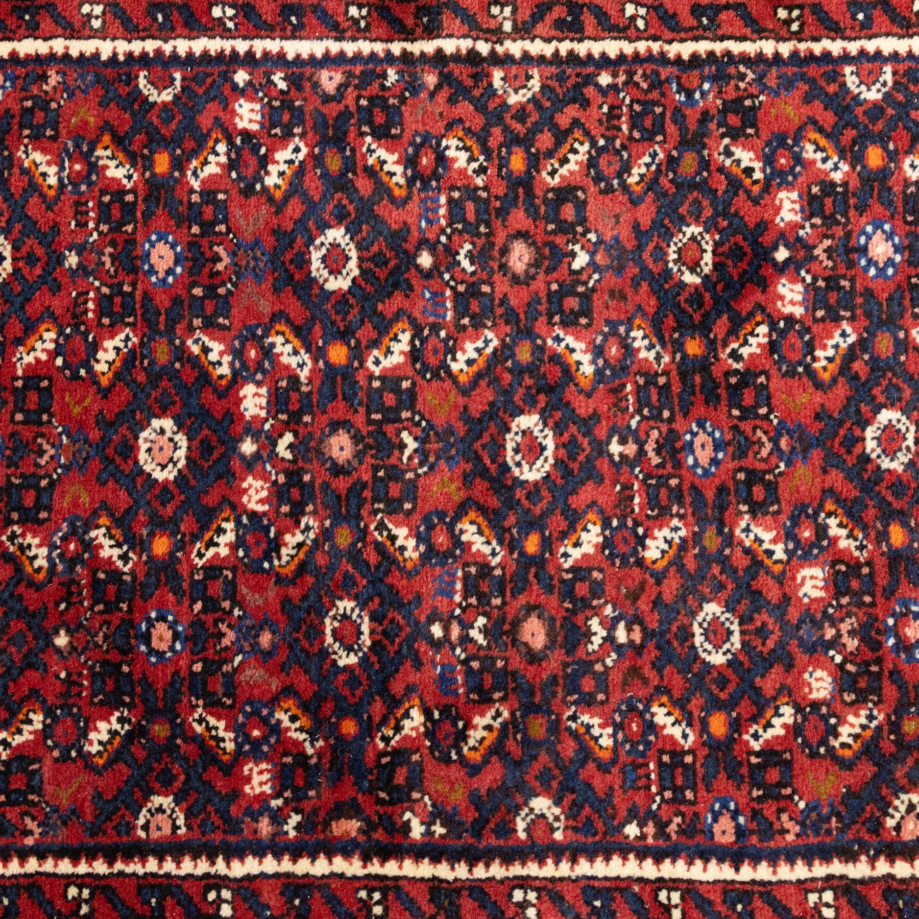 North West Persian Malayer hand-knotted runner, decorated with a dense all-over pattern of small repeating boteh and rosette motifs on a rich madder red ground, field filled with geometric floral elements arranged in a lattice design, framed by a narrow main border and flanked by slender guard borders, with cotton fringe ends 