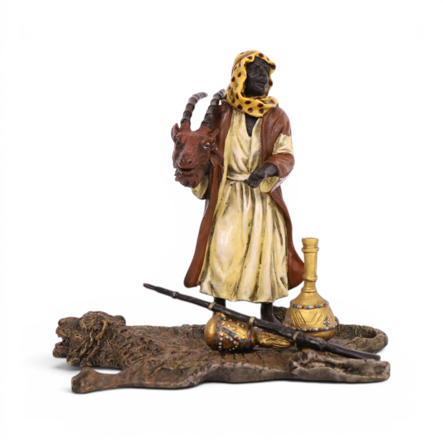 After Bergman - bronze Arab trader holding an antelope head while standing on a tiger skin, with a rifle and jars at his feet, H14cm