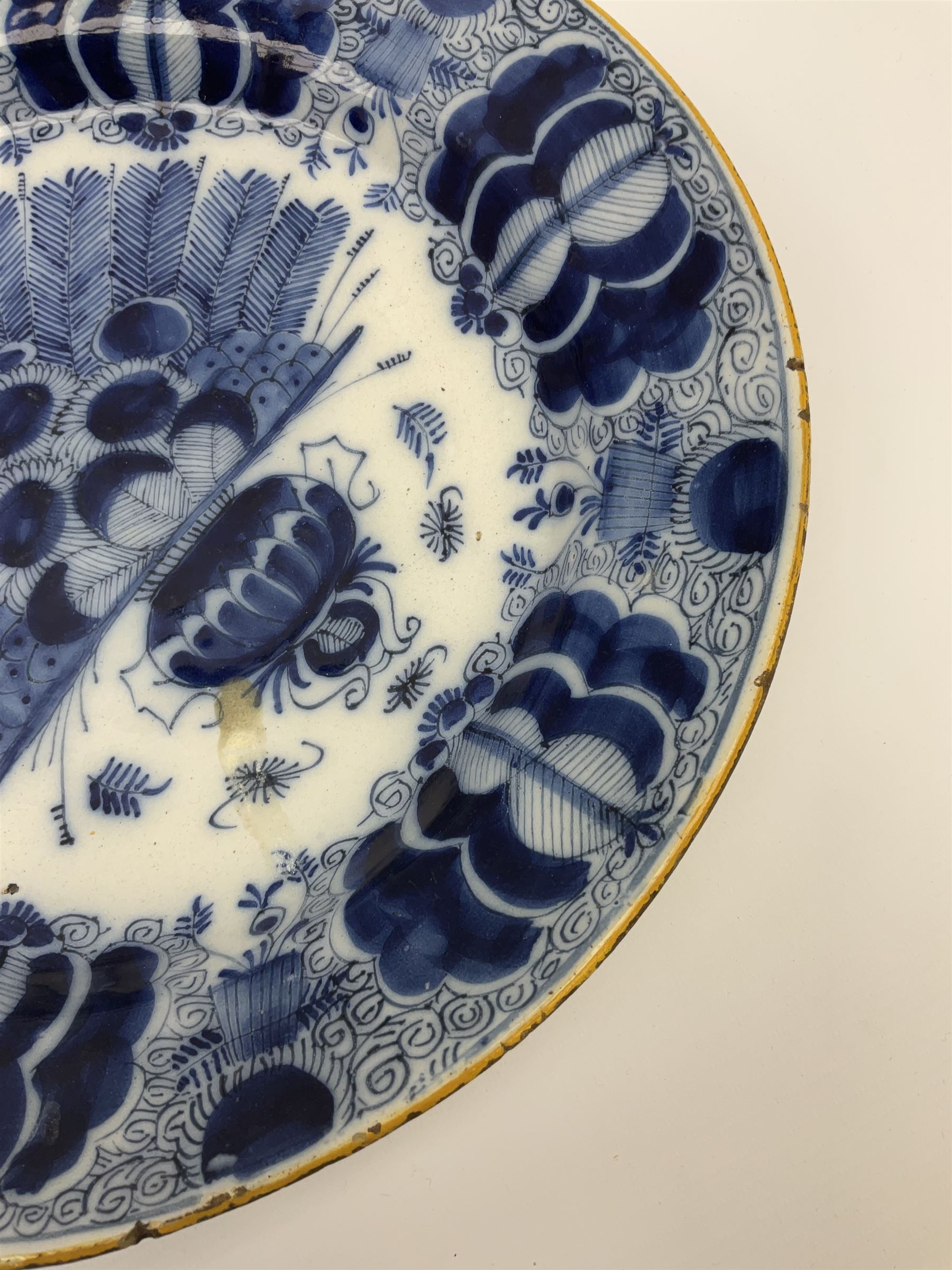 18th century Delft blue and white peacock pattern dish, painted with a fan of peacock feathers behind an urn of fruit and flowers, D34.5cm. 