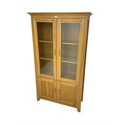 Light oak display cabinet, two glazed doors enclosing two glass shelves, over two panelled cupboards concealing single shelf