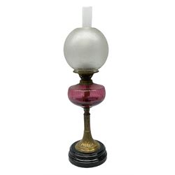 Victorian table standing oil lamp, brass fittings, cranberry glass reservoir, brass column on black enamelled ceramic base, with a frosted glass shade and clear glass chimney, H68cm