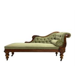 Victorian walnut framed chaise longue, the scrolled back carved with acanthus leaf and foliate motifs, the shaped rail applied with carved flower heads, upholstered in buttoned jade green fabric with bolter cushion, raised on turned supports with castors