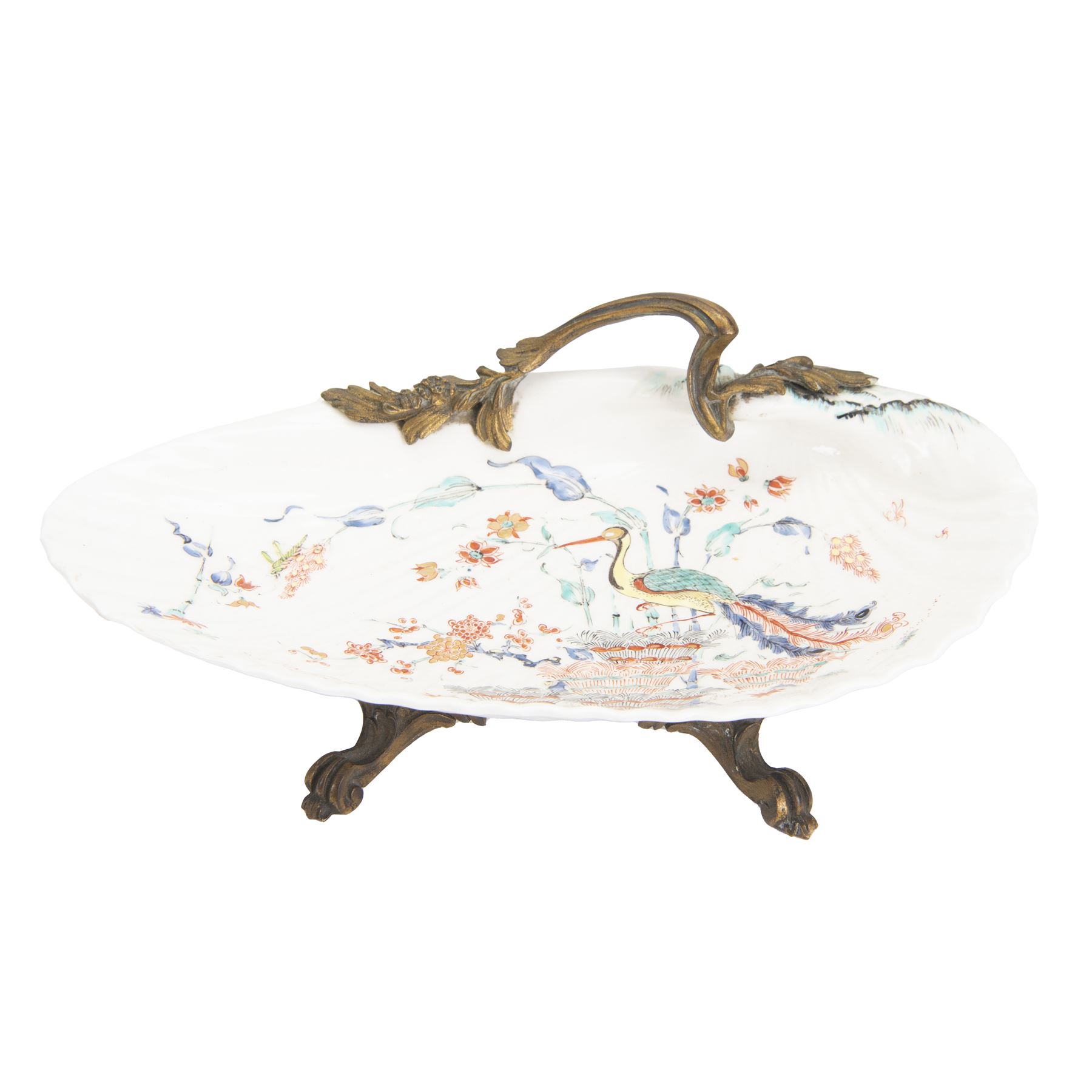 18th century porcelain dish, attributed to Chantilly, circa 1740-1750, with later ormolu mounted handle and feet, the dish of moulded shell form, painted in the Kakiemon pallet with an exotic bird and grasshopper amidst flowers and foliage, with foliate ormolu handle, and upon three scrolling foliate feet, possible obscure Chantilly mark beneath, including handle H10cm W31cm

A letter from the Ashmolean Museum accompanied the dish when it entered the current vendor's family collection. In the letter, Dr. Impey noted that the painting is European, possibly Dutch. The general consensus was that the shell dates to the 18th century, with the ormolu mounts likely added in the 19th century. However, the factory of origin remained unidentified. The letter was signed by Ian Lowe in 1974. Further consultation at the time with four members of staff at the Victoria and Albert Museum yielded differing opinions, with suggestions including Chantilly and Bow. The piece has been attributed to Chantilly partly due to what appears to be a partially obliterated horn motif beneath.