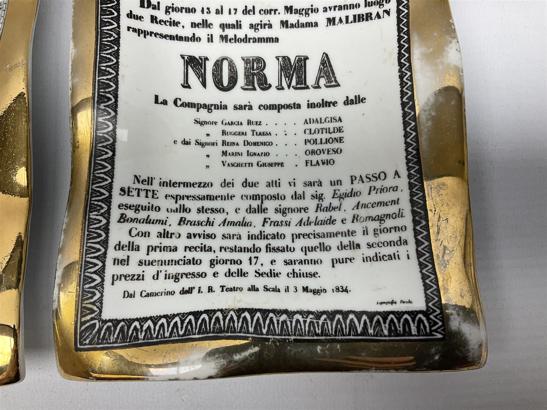 Two Fornasetti rectangular operatic posters ashtrays 'Norma' and 'Iris' decorated with black and white text with a gilt border edge, with printed mark beneath, H16cm