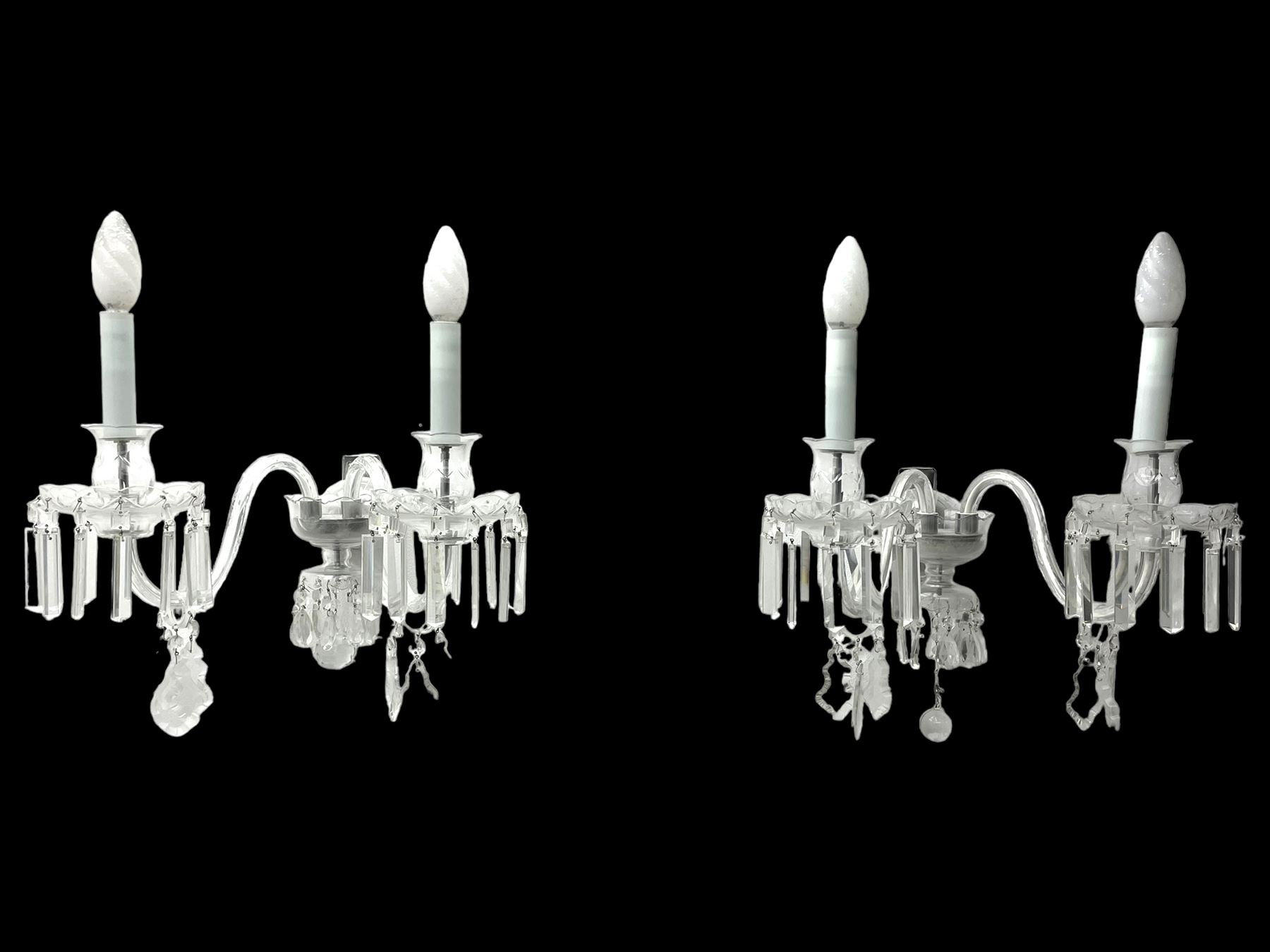 Pair of cut glass two branch wall sconce candelabras, each with S scroll extending branches with shaped and bevelled circular drip trays, hung with pendant drops