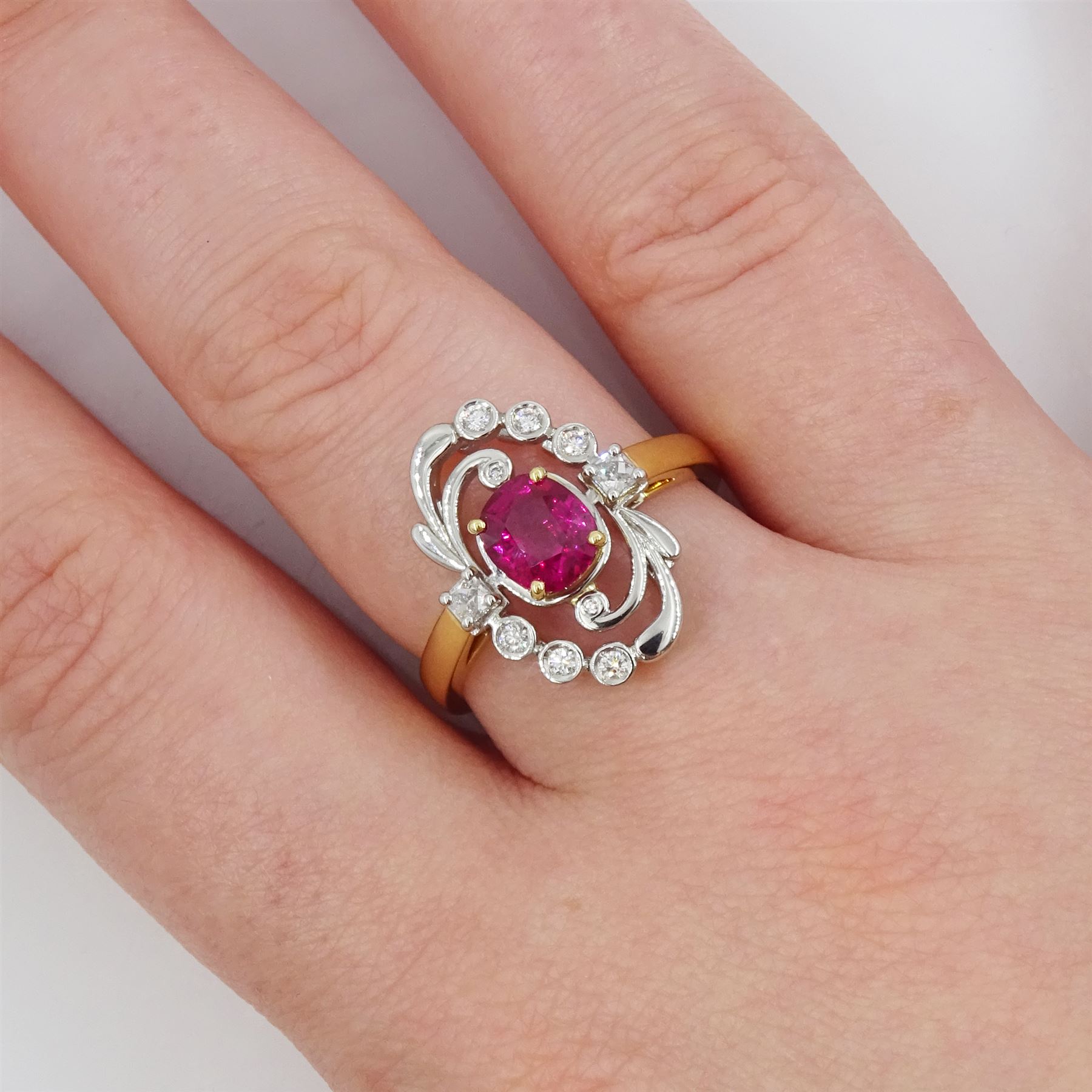 18ct gold and platinum Burmese ruby and diamond ring by Scarab London, single rectangular cushion cut unheated ruby of 1.13 carat, with a single French cut diamond set either side and round brilliant cut diamond surround, in a scrolling foliate design setting, with Alan Poultney Gems report, the ruby with The Gem & Pearl Laboratory report