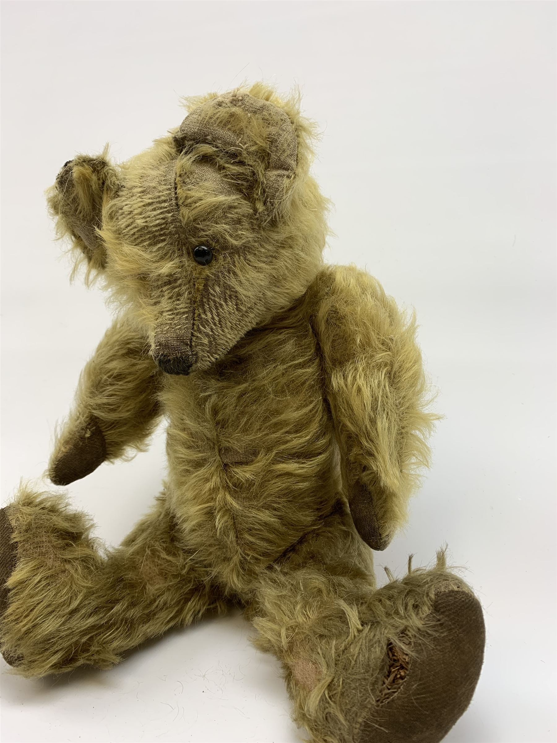 Early 20th century English teddy bear, WW1 period, with wood wool filled mohair body, fixed head with one boot button eye and vertically stitched nose and mouth and jointed limbs with cloth paw pads H16
