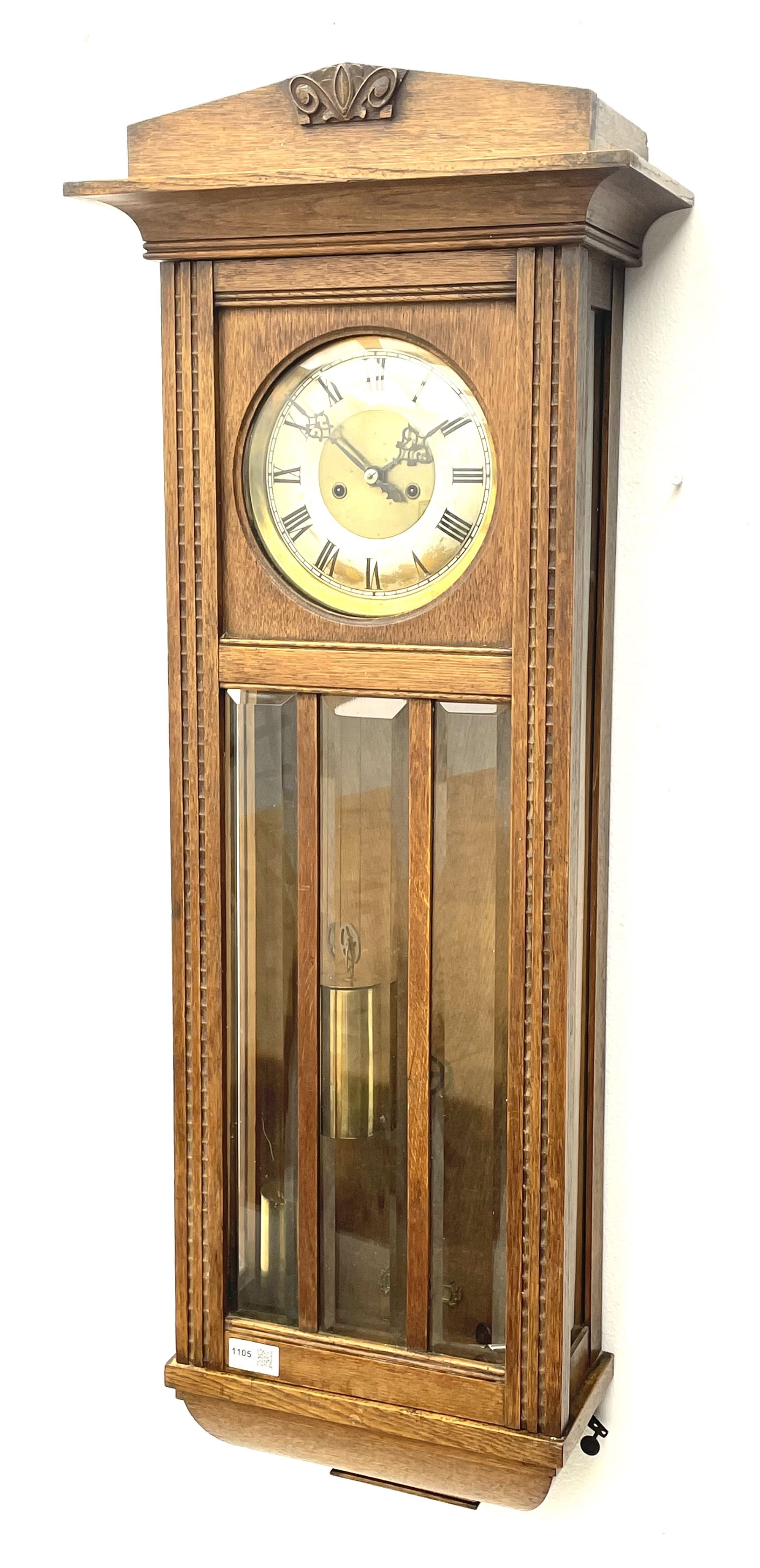 Early 20th century oak cased wall clock, the door glazed with circular convex dial glass and bevelled upright panes, circular brass and silvered Roman dial, twin train driven movement striking on coil 