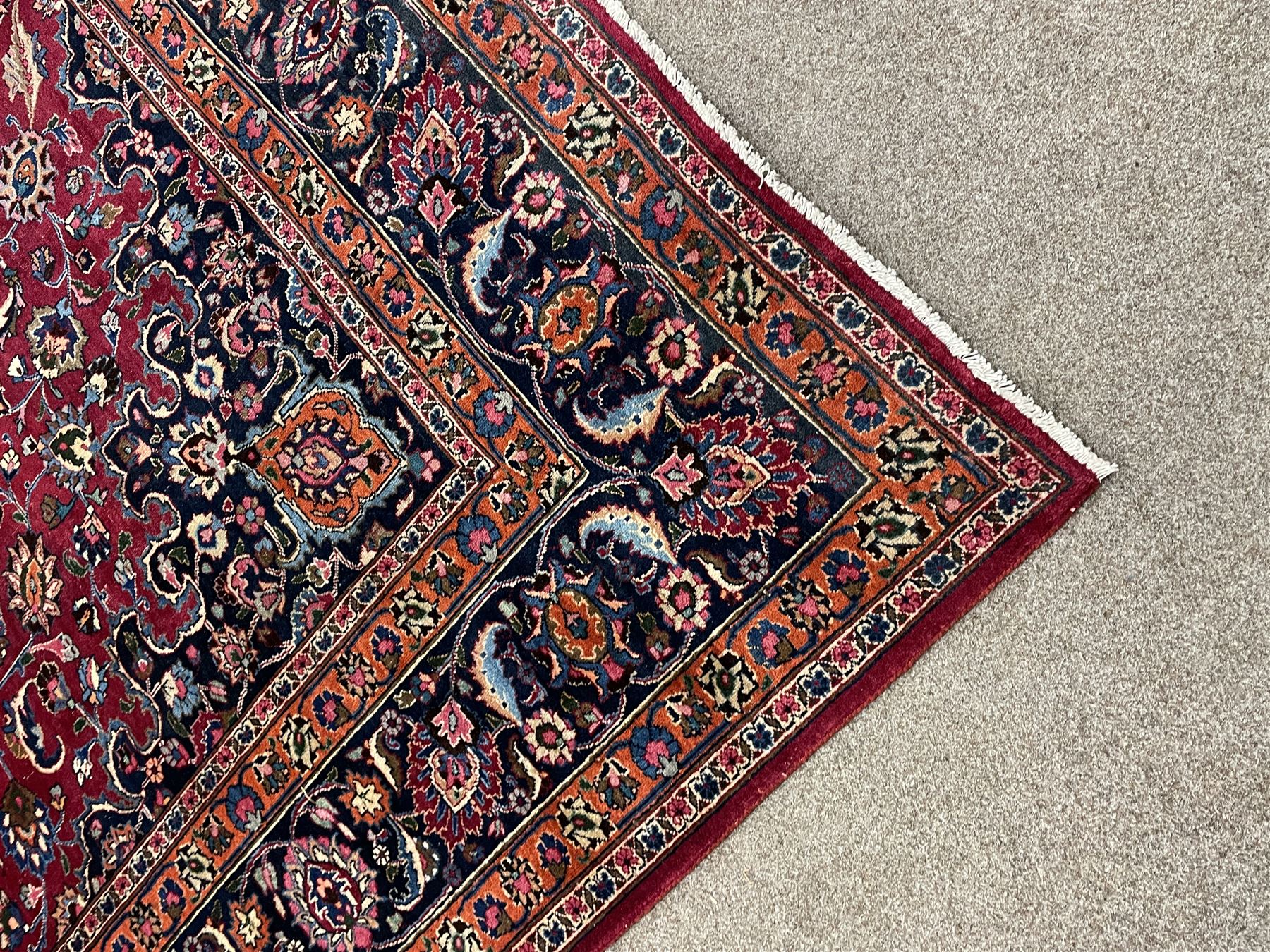 Persian Meshed carpet, plum ground and decorated with stylised flower heads and interlacing foliate, large central stylised medallion with orange detail, the orange mirrored in the five band border decorated with scrolling floral design, signature panel to end 