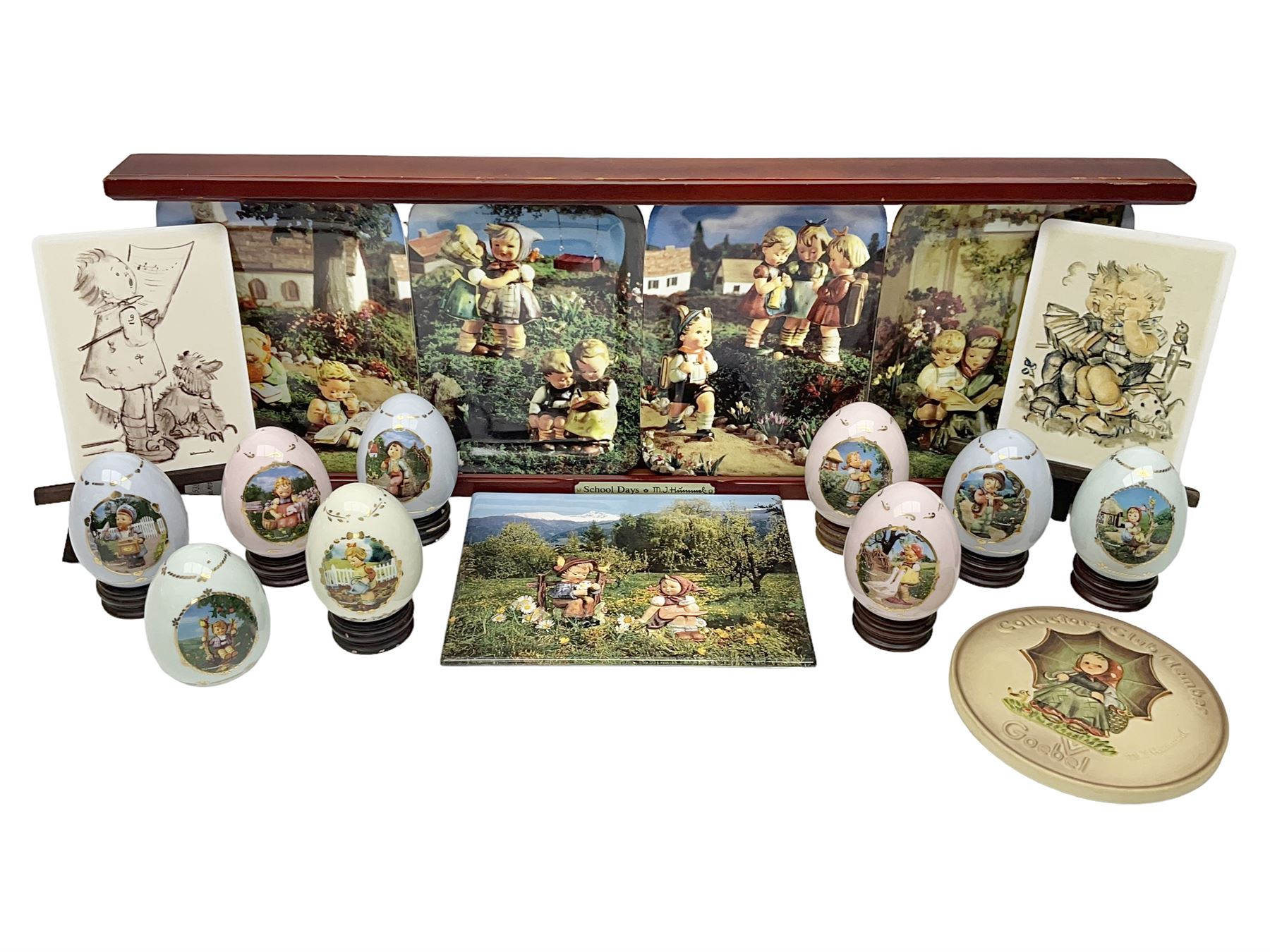 Two ceramic Hummel postcards by Goebel, both displayed on wooden easels, together nine Hummel eggs, set of four Hummel School Days plates, on wooden hanging rack, Goebel Collectors Club Member plaque etc