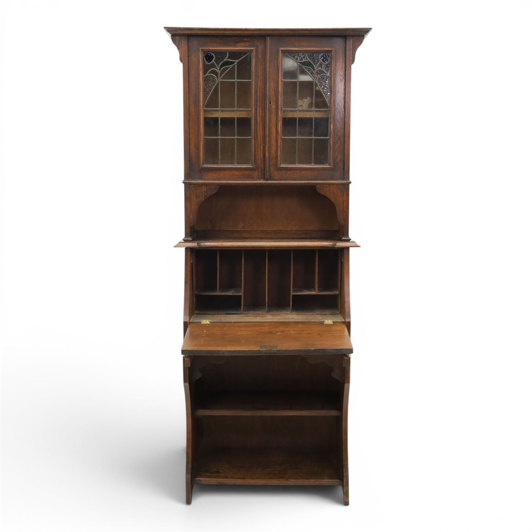 Arts & Crafts oak bureau bookcase, projecting cornice with leaded and glazed upper cabinet, the lower section with fall front section revealing a fitted interior, above shaped lower shelving 