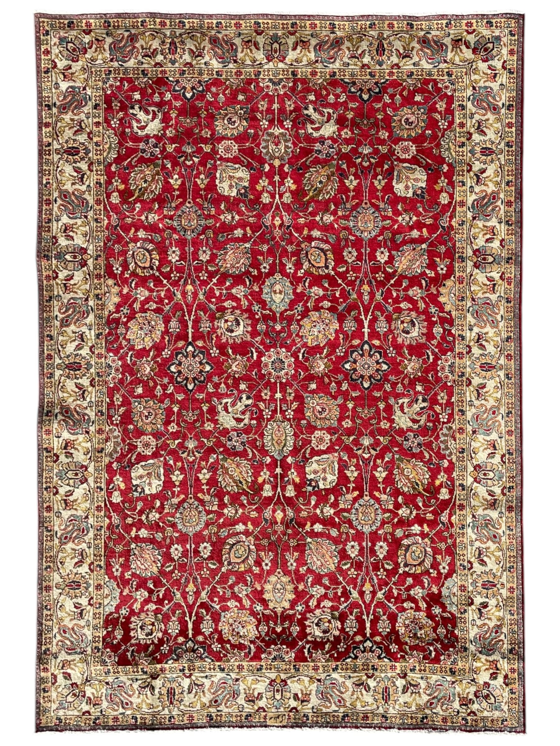 Persian Tabriz crimson ground rug, the field decorated with large palmette and stylised plant motifs connected by interlaced leafy branches, trailing border decorated with similar palmette motifs within floral pattern guard stripes, with signature panel 