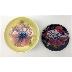 A Moorcroft dish, decorated with the Clematis pattern upon a yellow ground, with paper label beneath, D14cm, together with a Moorcroft pin dish, decorated with the Clematis pattern upon a dark blue ground, with incised marks beneath, D11.5cm, with maker's box. 
