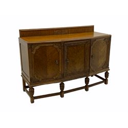 Early 20th century carved oak sideboard, the raised back carved with scroll work over angled moulded top, enclosed by three doors carved with trailing foliage and berries, the central cupboard fitted with four drawers, on baluster carved supports joined by moulded stretchers
