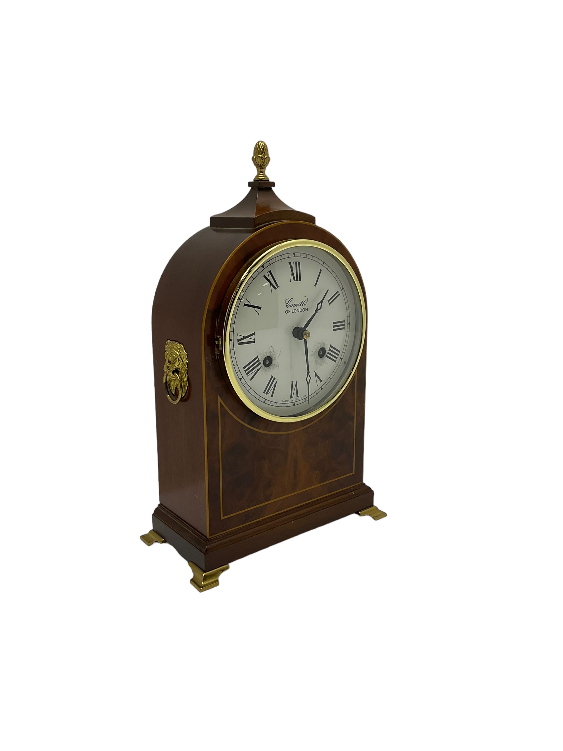 Comitti of London - 20th century 8-day mantle clock, in classic round topped mahogany case with inlaid stringing to the front and lion mask handles to the sides, raised on a narrow plinth with bracket feet, twin train going barrel movement with a floating balance escapement, striking the hours and half hours on a bell.    