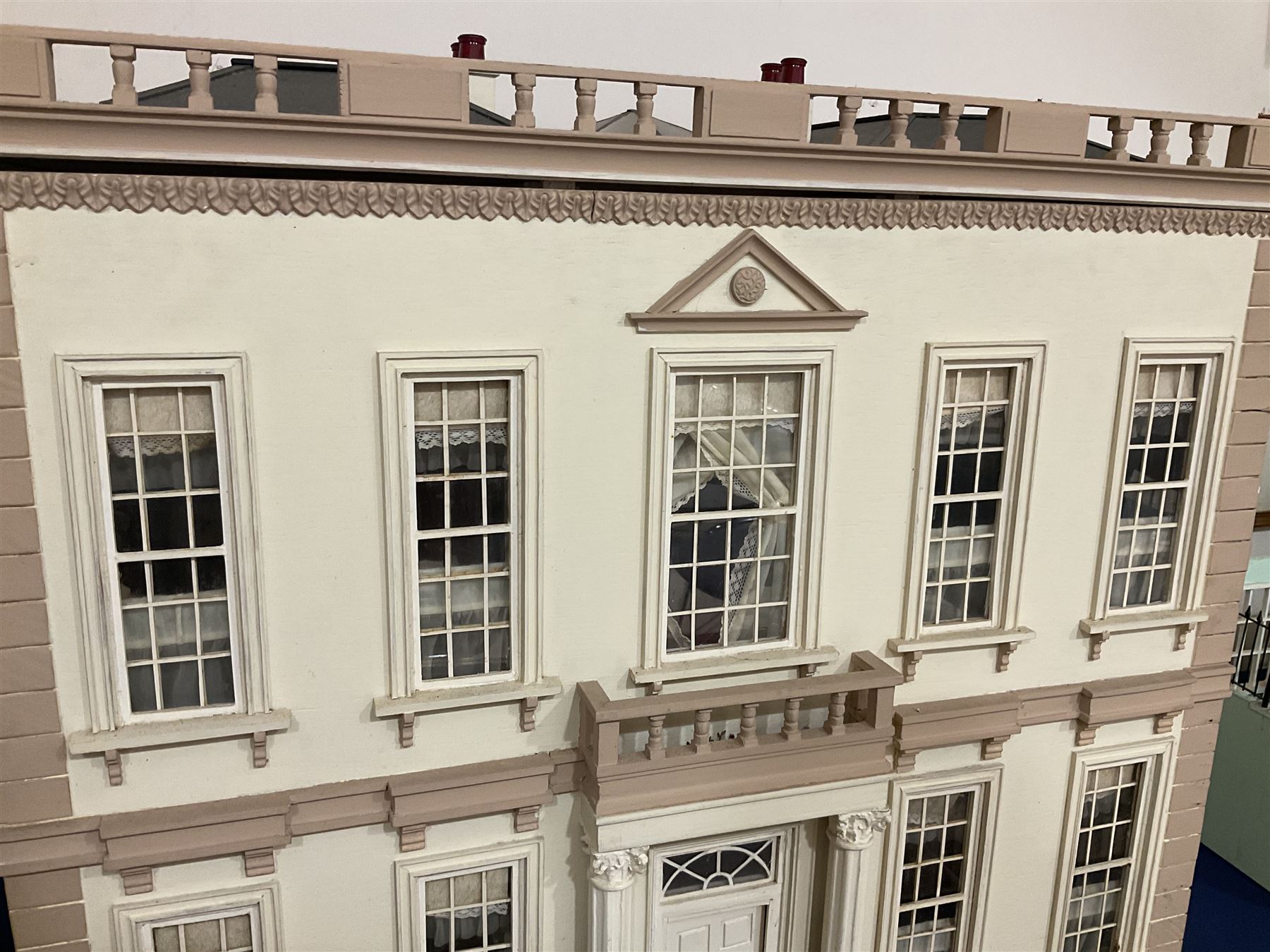 Kit-built wooden dolls house, possibly by Honeychurch, as a 19th century style double fronted two-storey residence; with stucco walls and flat roof with circular skylight and parapet with balusters; central door with fanlight, Corinthium columns and balcony over; simulated sash windows to three sides; hinged front facade opening to reveal a partially furnished interior with central hall, stairs and landing, two ground floor rooms and two first floor en suite bedrooms; wired for electric lighting W69cm H70cm D41cm