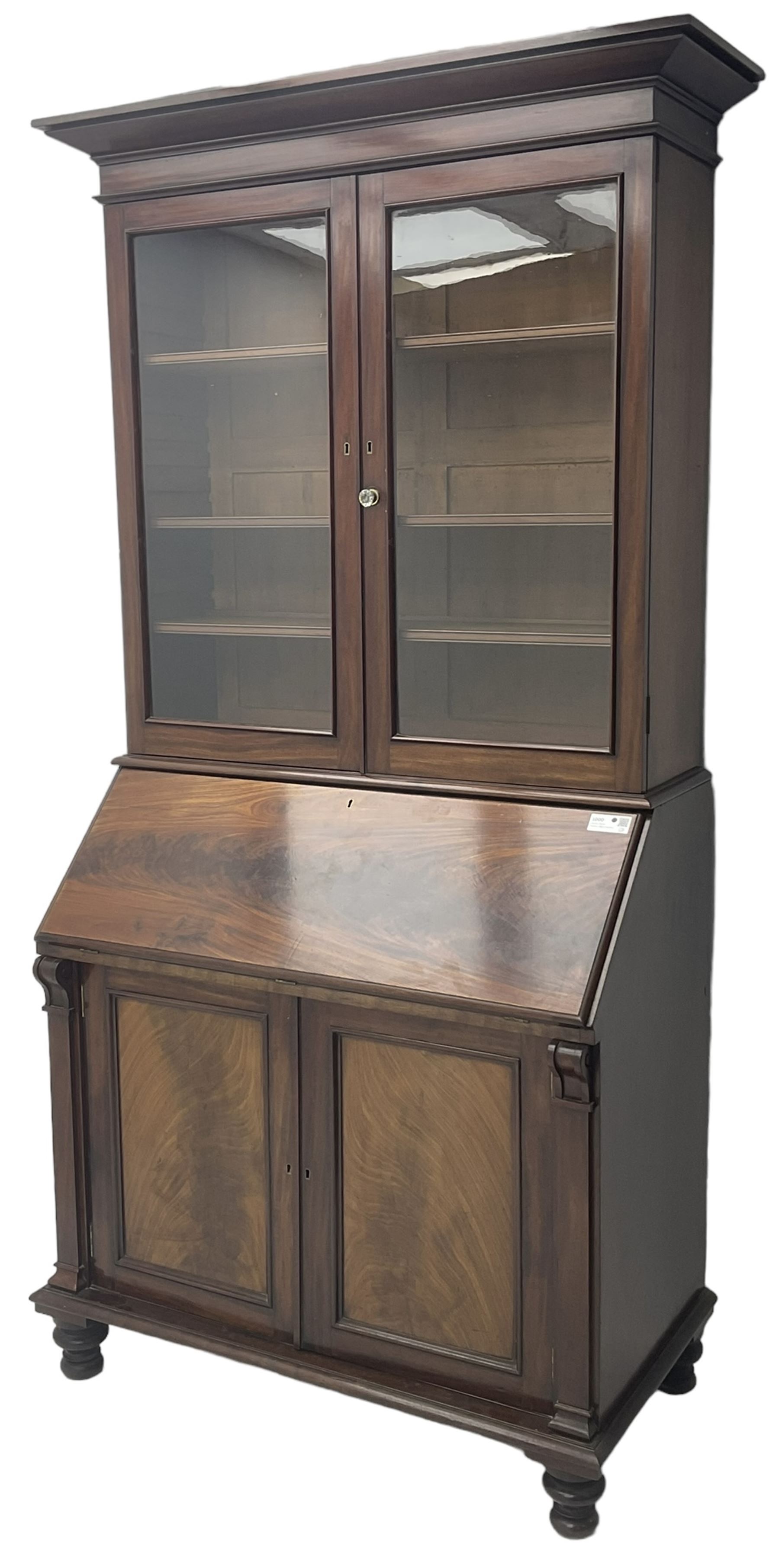 Early 19th century figured mahogany bureau bookcase, projecting splay moulded cornice over three adjustable shelves enclosed by two glazed doors, fall front revealing pigeonholes, cupboard and drawers, pull-out strays with scroll carved terminals, double cupboard with two panelled doors, on turned feet 