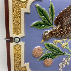 19th century Minton & Co majolica tile, decorated in relief with a bird upon a fruiting branch against a blue ground, with textured ochre border and anthemion to each corner, impressed mark verso, H19.7cm