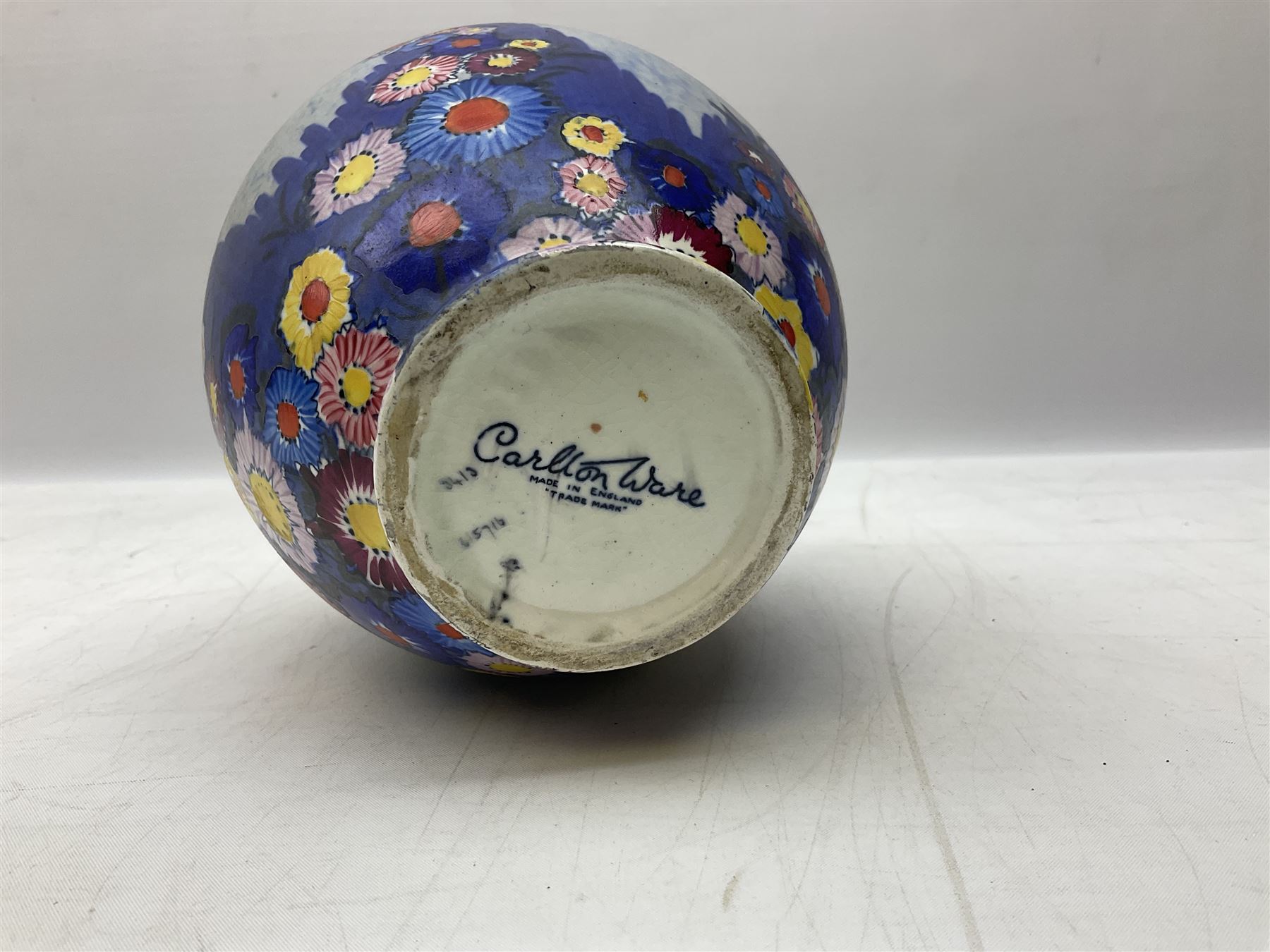 1930s Carlton Ware Art Deco Garden pattern vase of shouldered ovoid form, decorated with blue, pink and yellow flower heads on a mottled blue and white ground, pattern no. 3413, with printed and painted marks beneath, H19cm, together with a Clarice Cliff My Garden pattern vase, raised upon three feet with blue, pink and purple moulded Hollyhock design, H20cm, with Clarice Cliff Wilkinson Ltd England marks beneath