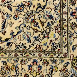 Central Persian Kashan hand-knotted rug, ivory ground, with a small central floral medallion and pendants, the field finely decorated with blue, cream and soft red scrolling vines, flowerheads and palmettes, within an ivory floral border and narrow guard stripes, with cotton fringes