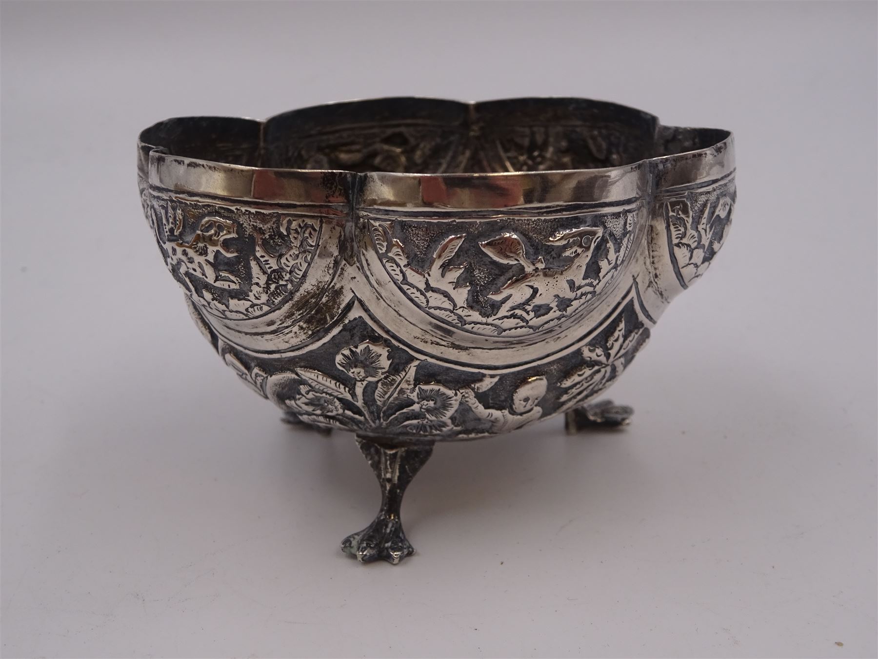 Continental silver bowl, of circular lobed form, repousse decorated with tribal and hunting scenes, upon three claw feet, unmarked but testing as 800 silver, H5cm, together with Chinese silver purse, of domed rectangular form, with ornate repousse decoration, depicting flowers, instruments, birds etc, with lobed wire wrapped handle, with Chinese character marks beneath, testing 650 silver,  including handle H11cm, and two base metal miniature animals