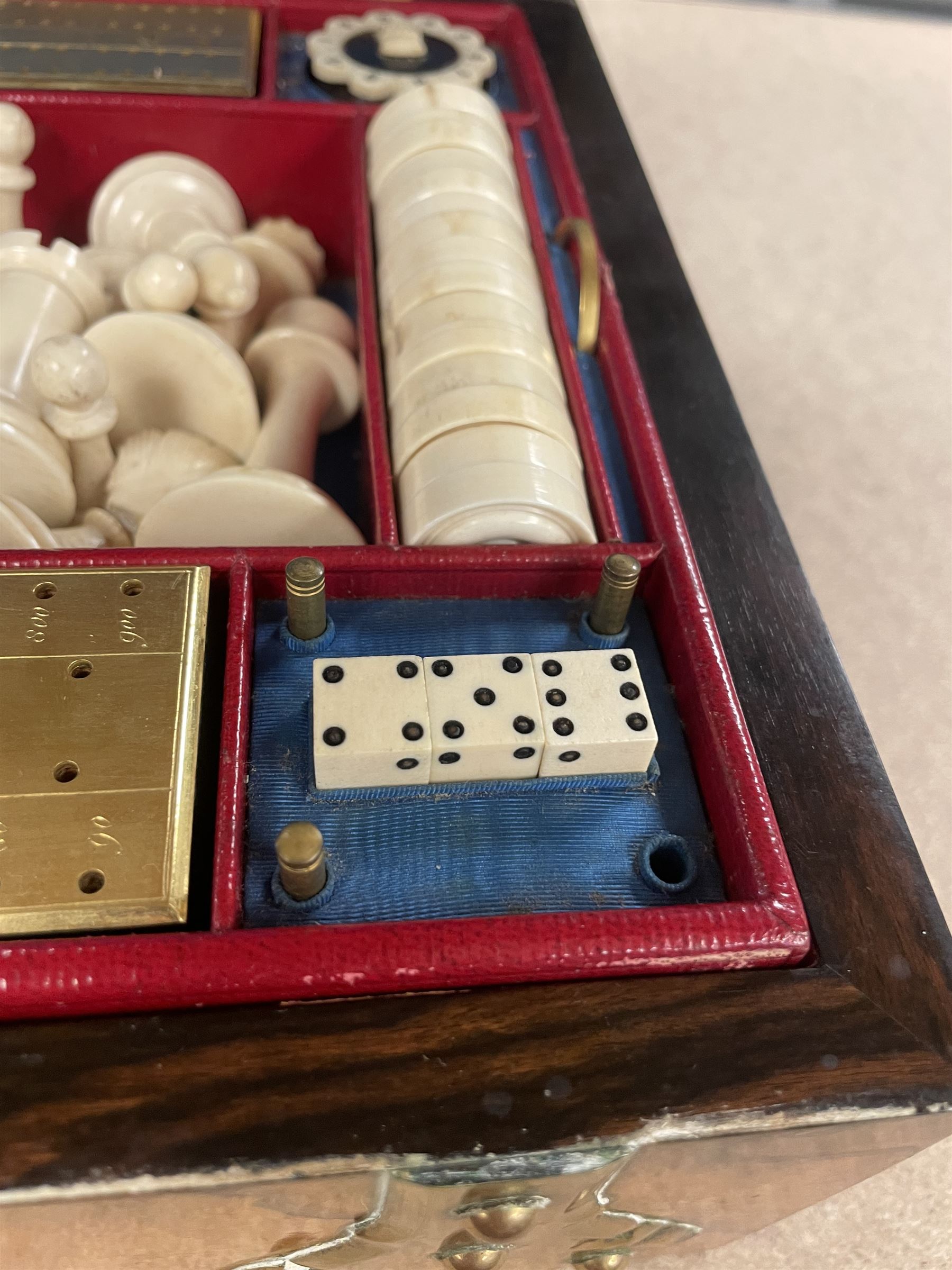 19th century walnut and brass bound games compendium box, painted to enhance the grain, of rectangular form, the hinged opening cover with rounded sides, central brass cartouche with engraved lion crest, and brass riveted straps, opening to reveal a red leather and blue silk lined compartmented interior, with fold-down games board, and lift-out tray containing playing cards, ebony turned dice towers, white and red stained bone draughts, and chess pieces, ivory dice, and ivory and ebony whist markers, and brass bezique board, cribbage board and markers, H15cm W32cm D24cm
This lot has been registered for sale under Section 10 of the APHA Ivory Act
