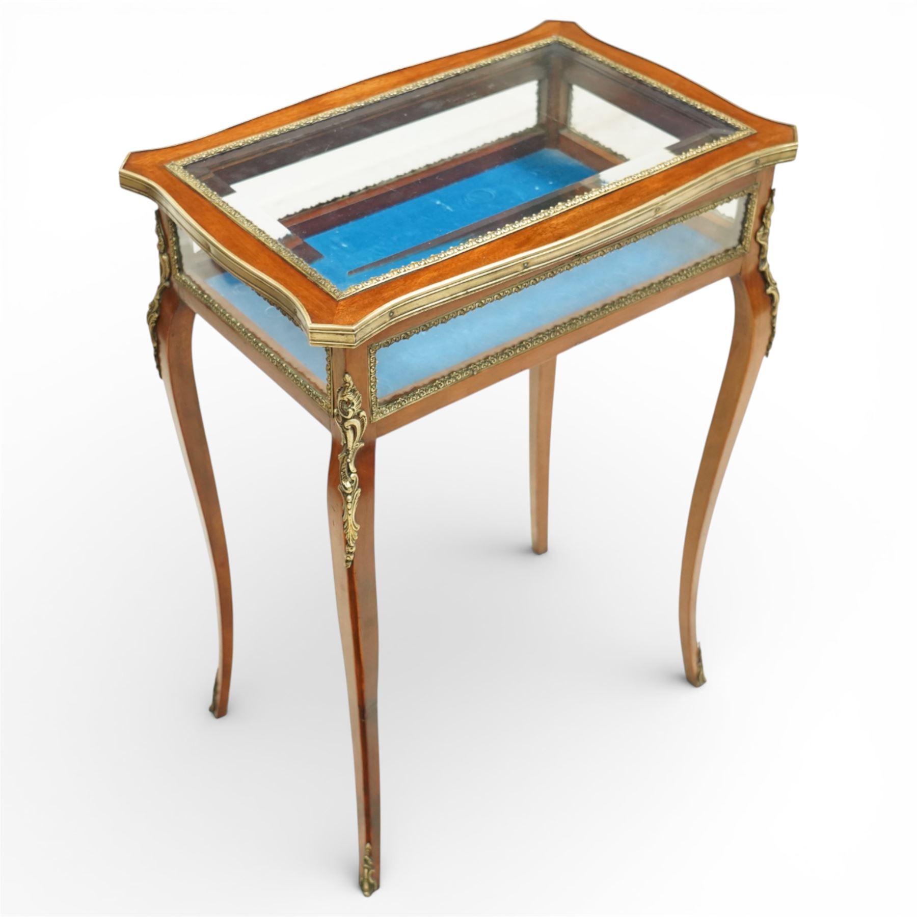 Early 20th century French mahogany bijouterie table, the hinged shaped rectangular top with brass edge and gilt-metal foliate slip enclosing bevelled glass plate, raised on cabriole supports with applied gilt-metal cartouche and foliate mounts